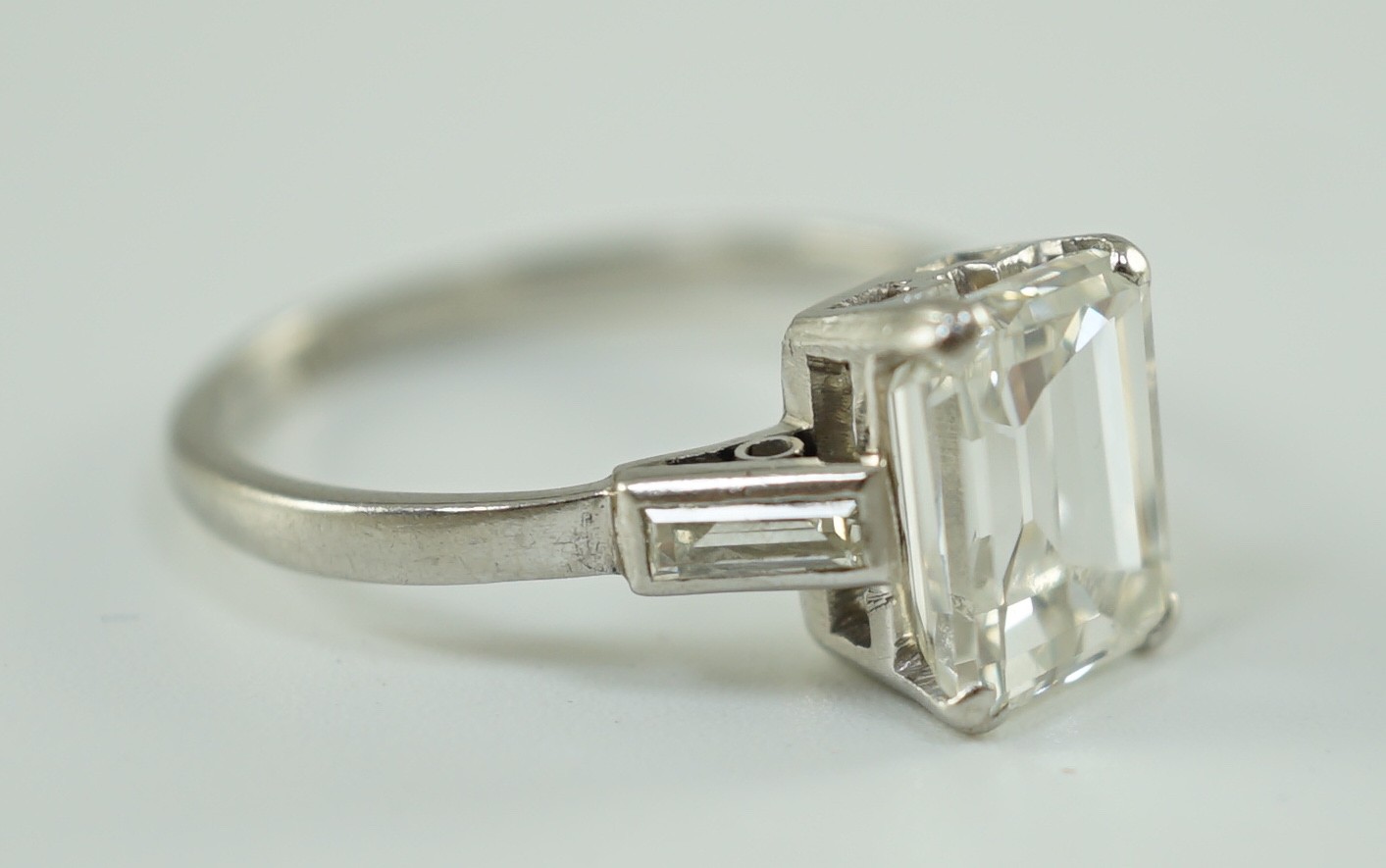 A platinum and single stone emerald cut diamond set ring, with baguette cut diamond set shoulders